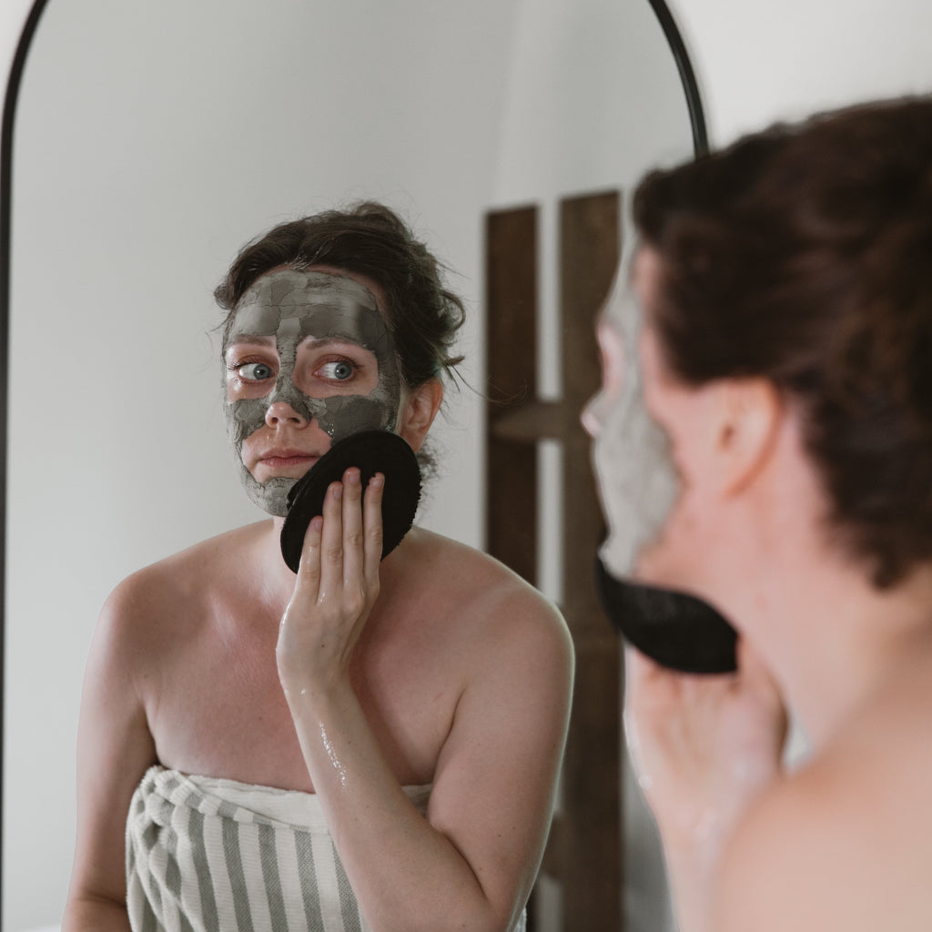 Oh Canada Gifts Ancient Mud Facial Mask applied to a woman's face, being removed with a black cleansing sponge.