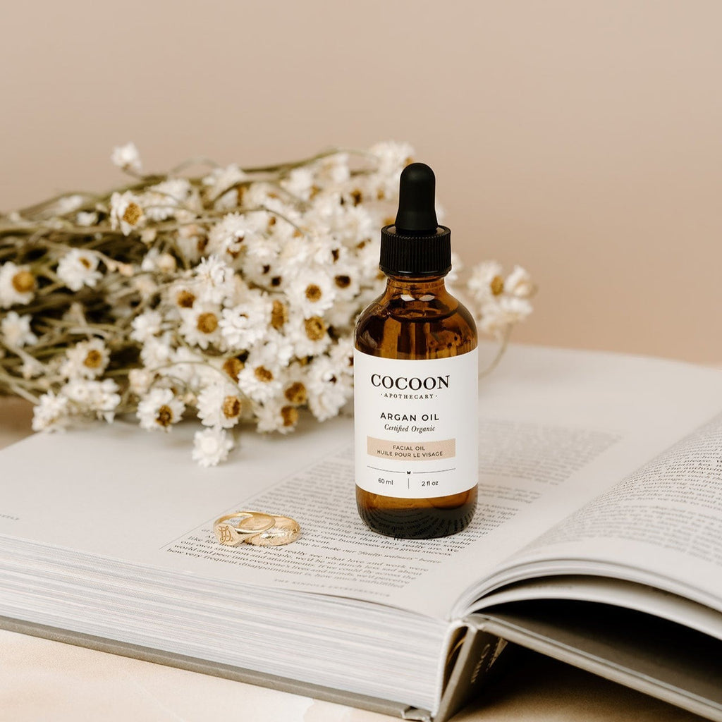 Oh Canada Gifts Argan Facial Oil in amber glass dropper bottle on an open book with dried white flowers