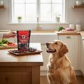 Oh Canada Gifts beef lung dog treats in a bag held by a hand, with a golden retriever waiting in a bright kitchen.