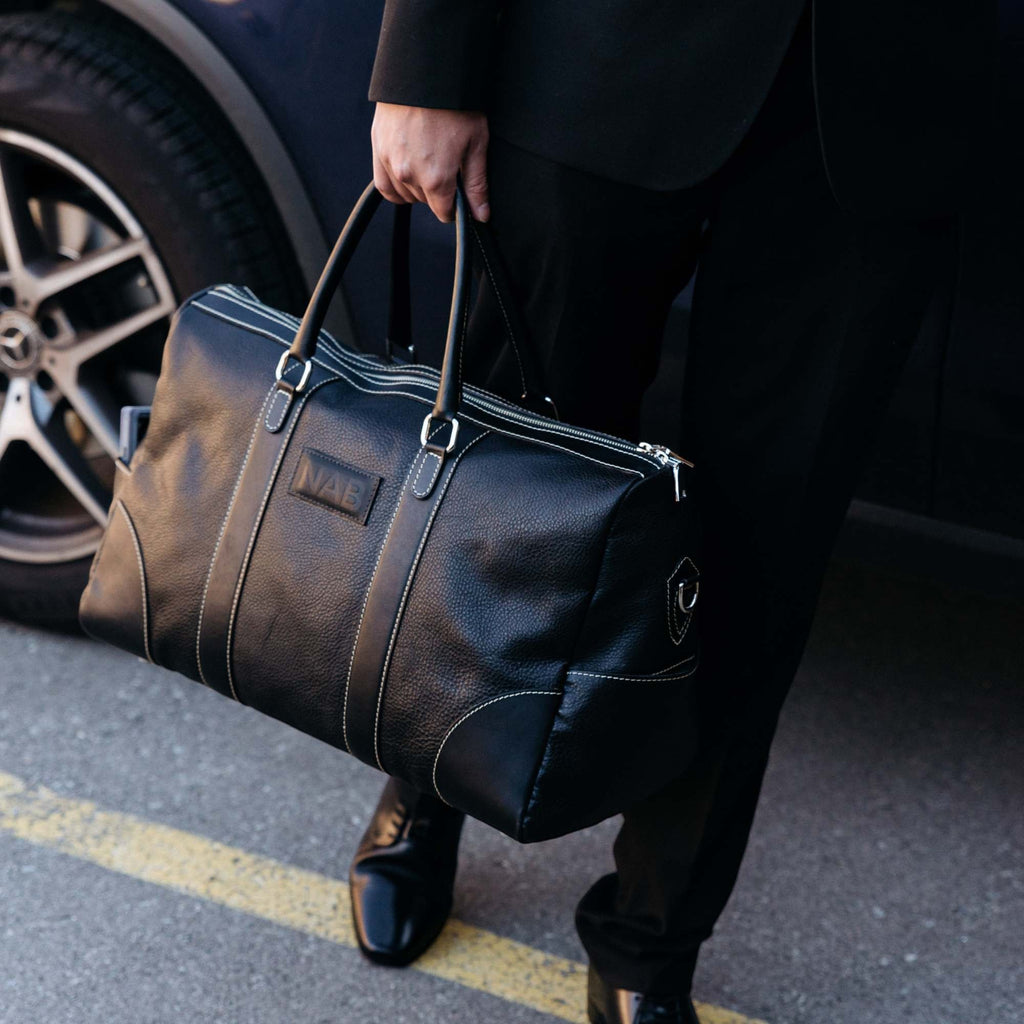 Oh Canada Gifts black full-grain leather duffle bag held by a person in a suit, showcasing handcrafted quality.