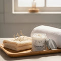 Oh Canada Gifts body lotion jar with a silver lid on a wooden tray next to a folded white towel and dried flowers.