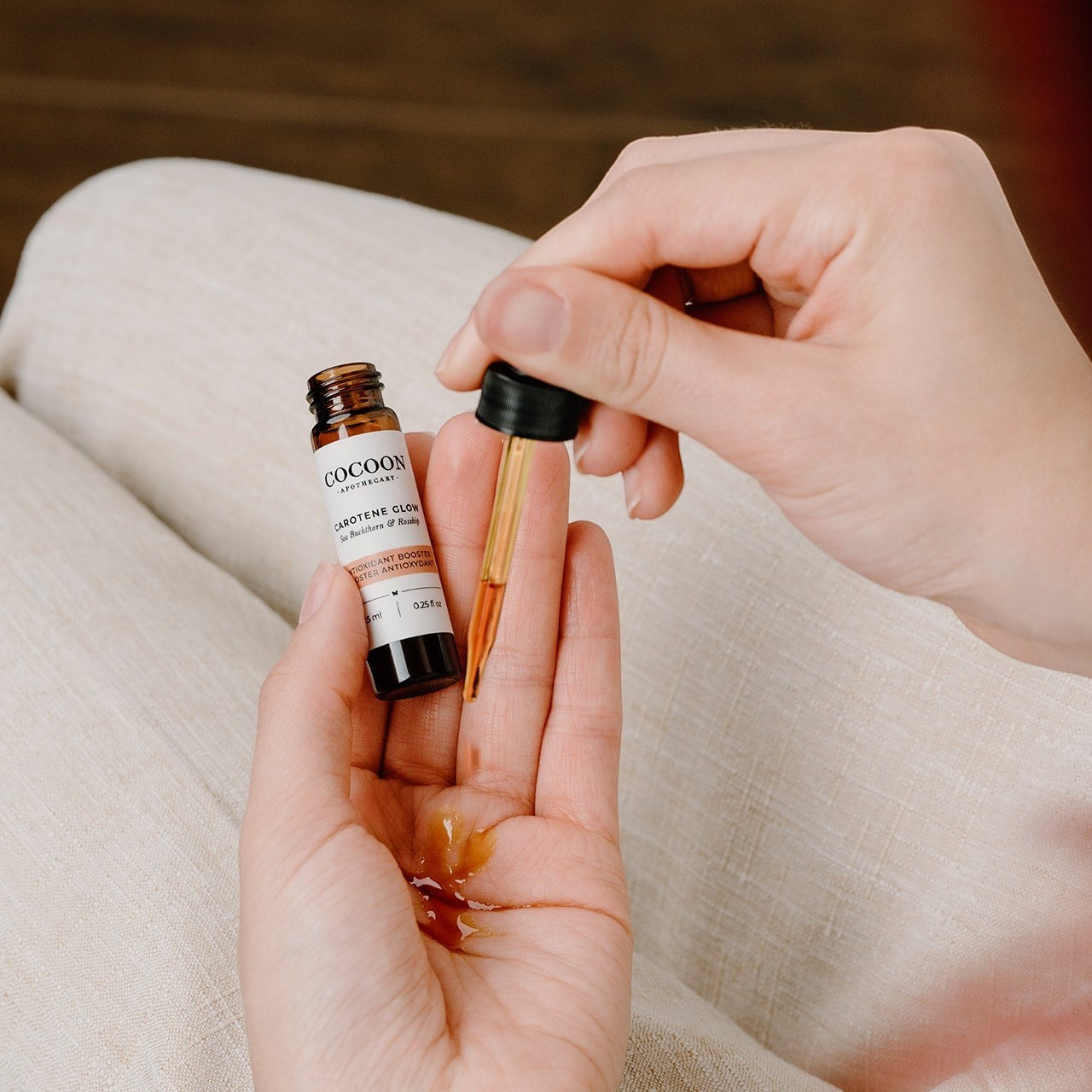 Oh Canada Gifts Carotene Glow facial serum in a small glass dropper bottle being applied to a person's palm