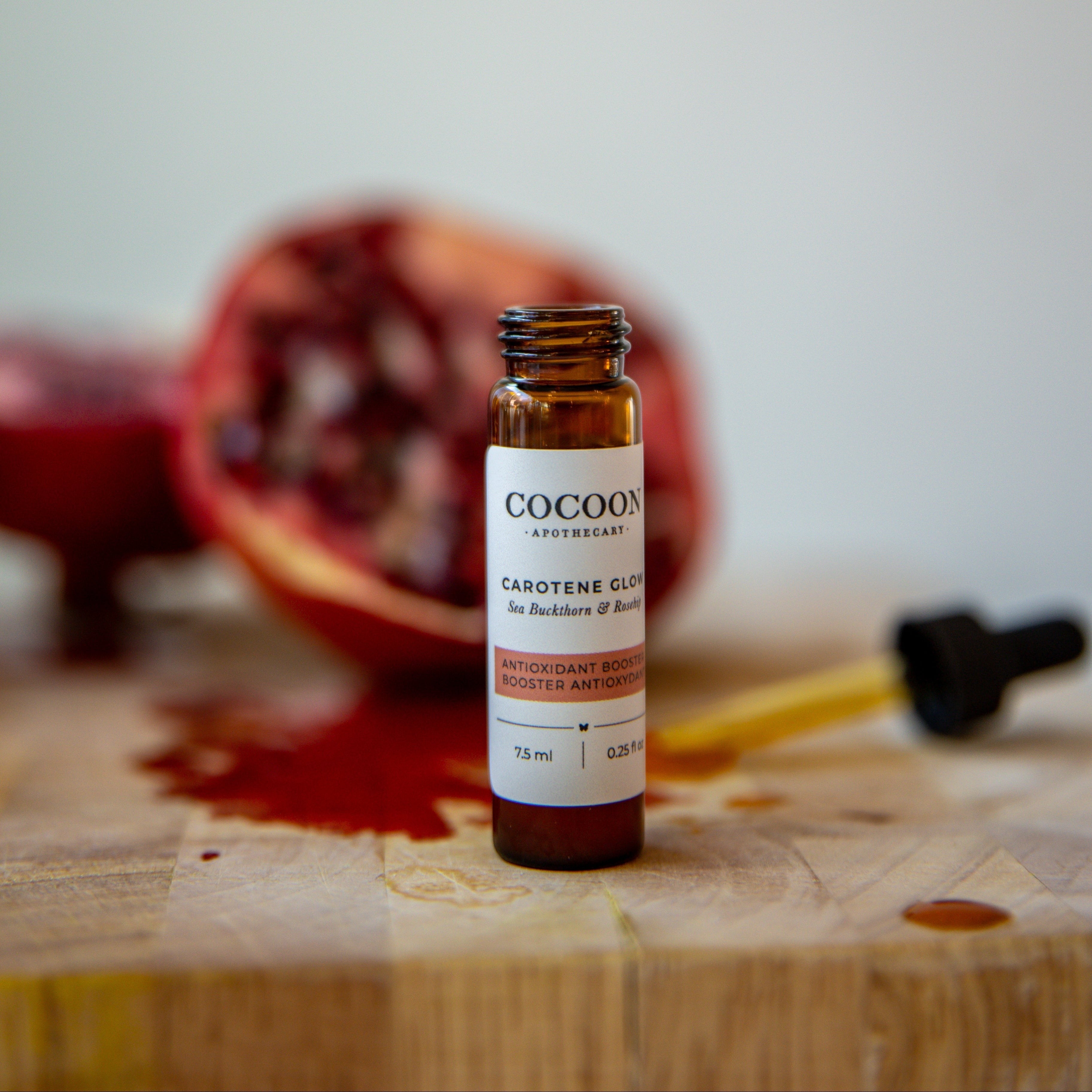 Oh Canada Gifts Carotene Glow facial serum in an amber glass bottle with a dropper, set against a sliced pomegranate.