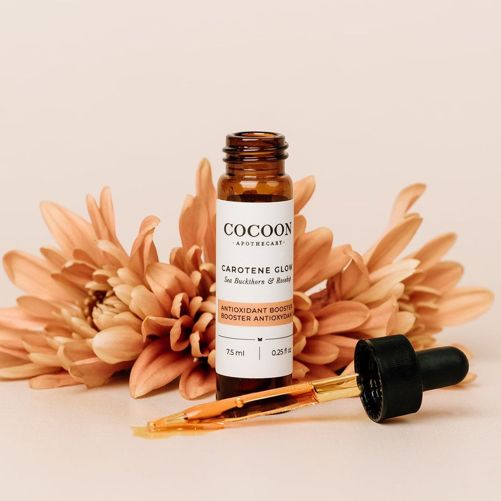 Oh Canada Gifts Carotene Glow Antioxidant Booster serum in an amber glass bottle with a dropper and orange flowers.