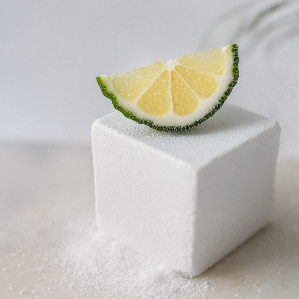 Oh Canada Gifts Citrus Tea Bath Cube topped with a fresh citrus slice on a white surface.