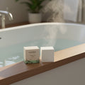 Oh Canada Gifts Citrus Tea bath cube beside its packaging on a wooden bathtub ledge with steam rising from warm water.