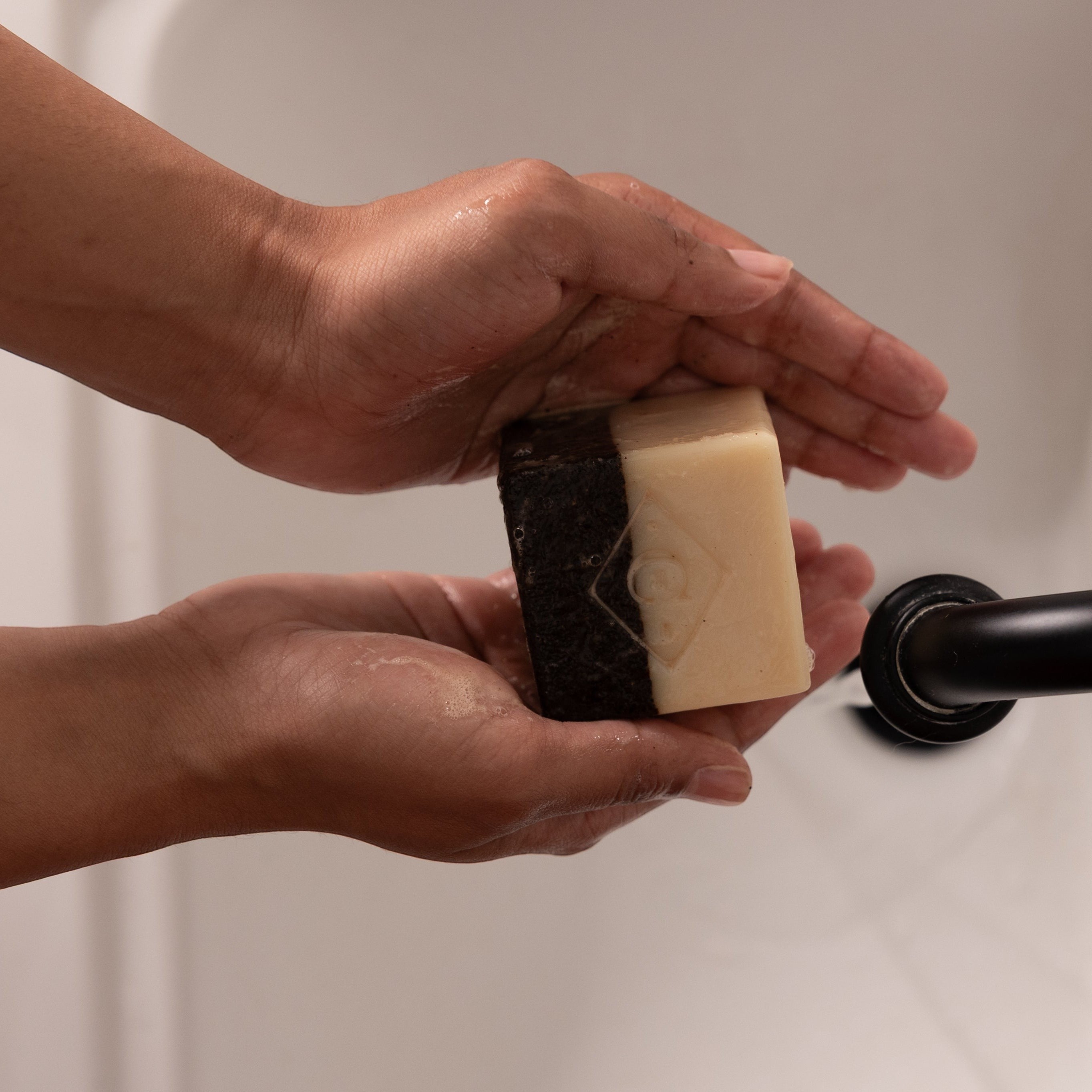 Oh Canada Gifts dual-action coffee scrub bar soap being held under running water for exfoliation