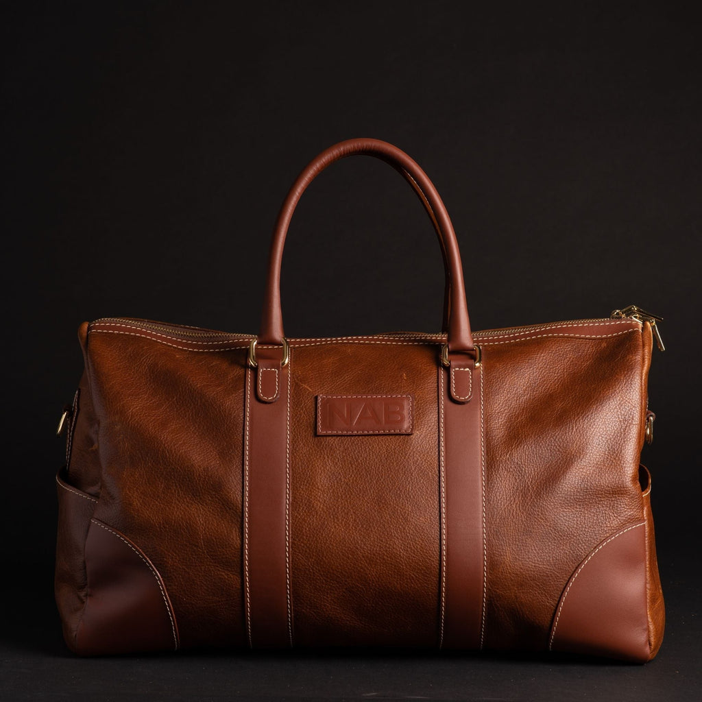 Oh Canada Gifts NAB Leather Shield duffle bag in cognac full-grain leather with reinforced handles and brass hardware.