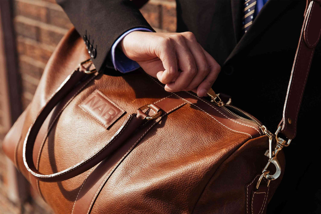 Oh Canada Gifts NAB Leather Shield duffle bag in cognac full-grain leather being opened by a person in a suit.
