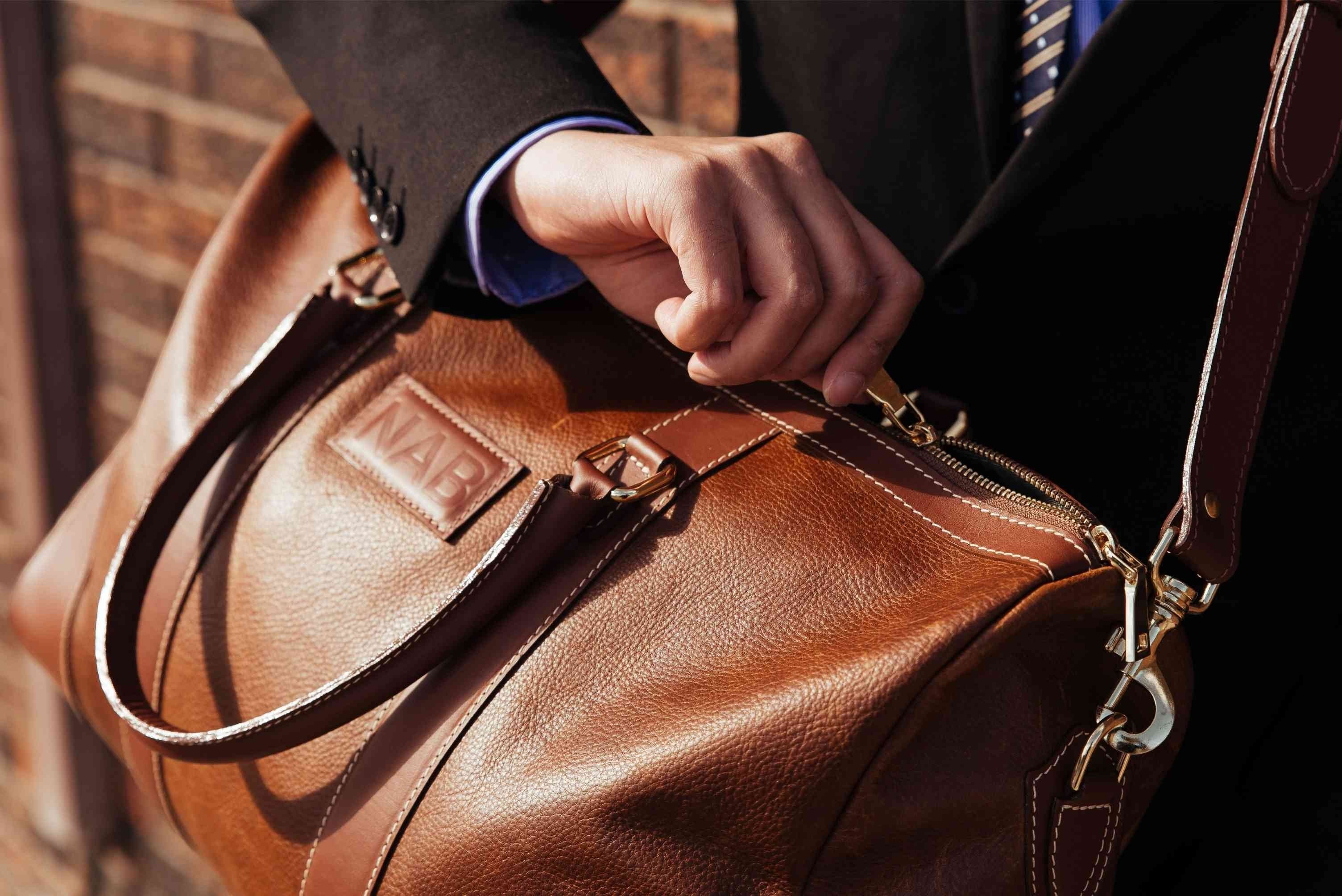 Oh Canada Gifts NAB Leather Shield duffle bag in cognac full-grain leather being opened by a person in a suit.