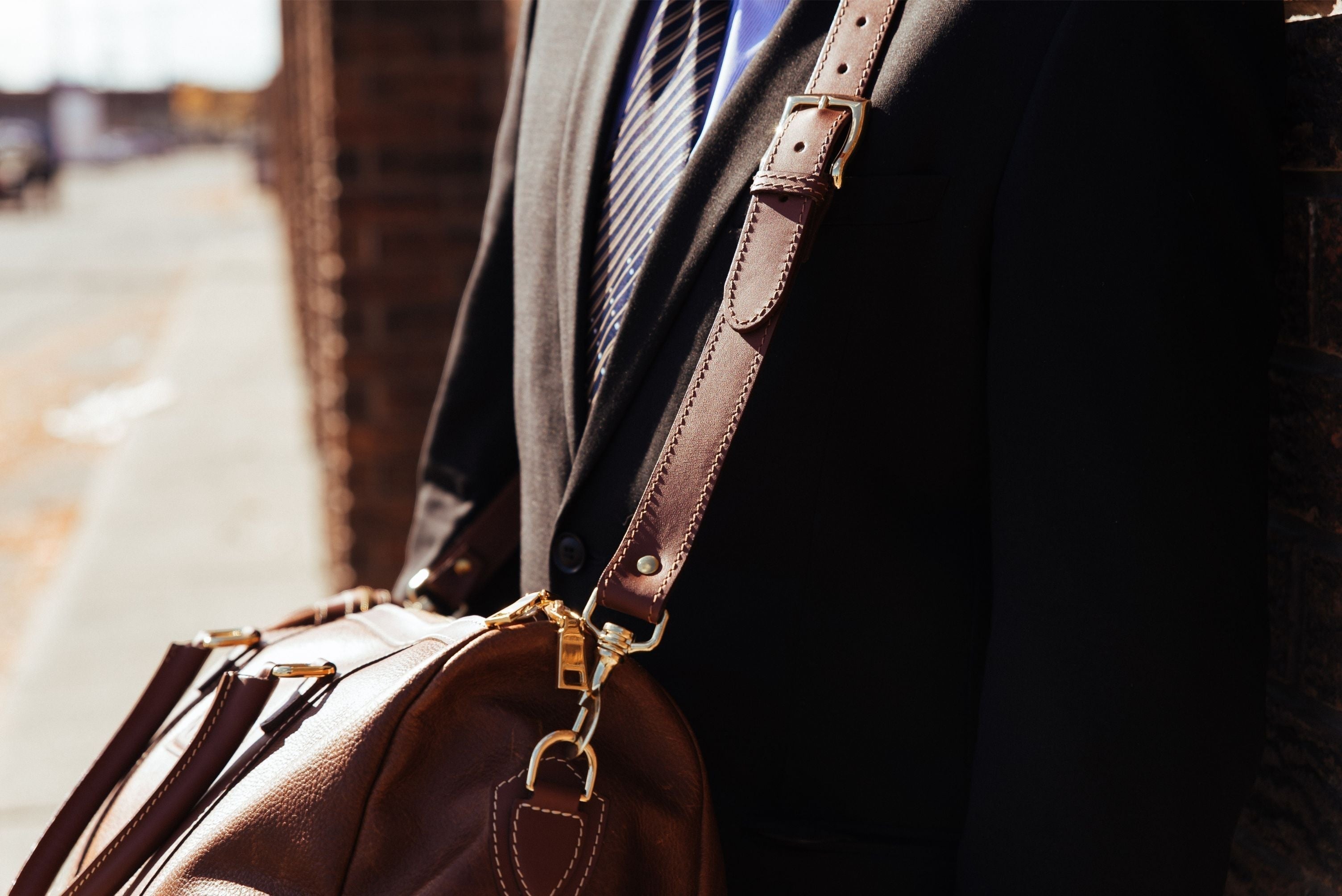 Oh Canada Gifts Shield Duffle bag in cognac full-grain leather worn over the shoulder by a man in a suit