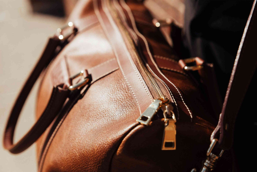Oh Canada Gifts Shield Duffle bag in cognac full-grain leather with gold-tone zipper hardware and detailed stitching.