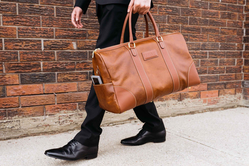 Oh Canada Gifts Shield Duffle bag in cognac full-grain leather carried by a man in a suit against a brick wall