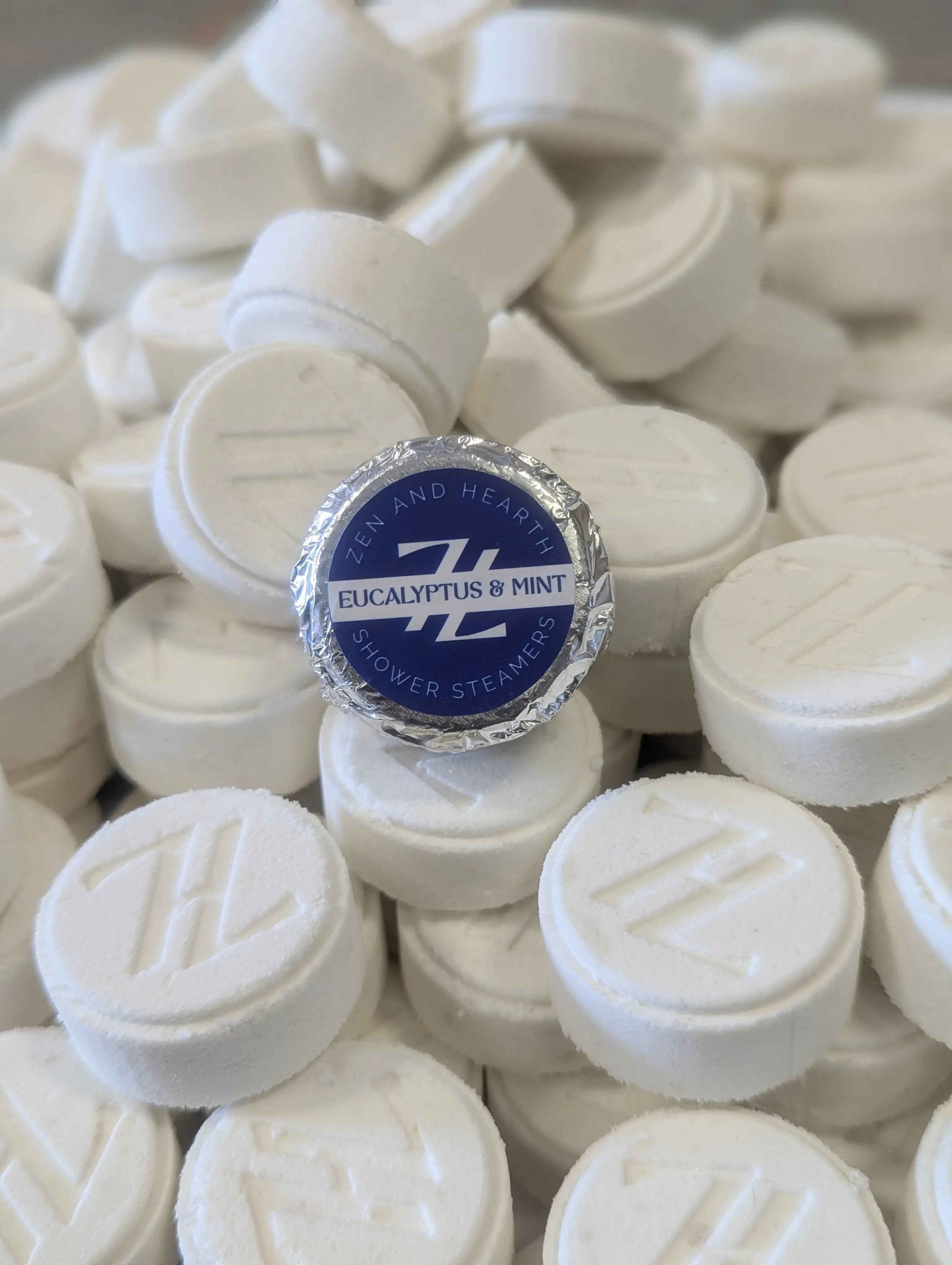 Oh Canada Gifts Zen & Hearth eucalyptus and mint shower steamer tablets with embossed logo on a pile of white discs.