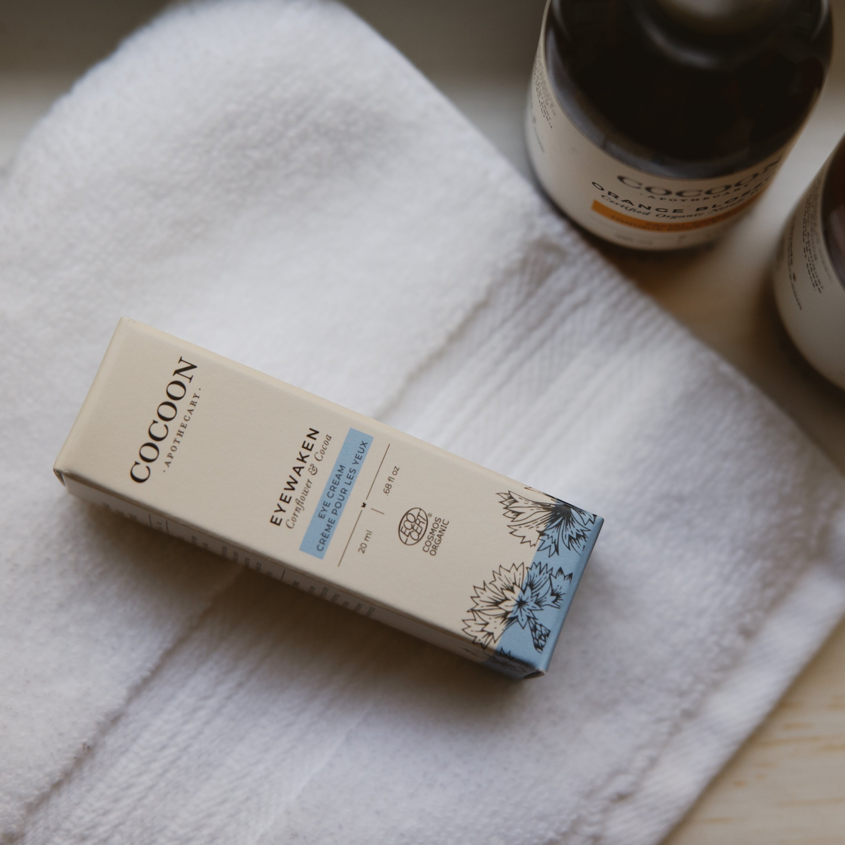 Oh Canada Gifts Cocoon Apothecary Eyewaken eye cream box on a white towel with botanical illustrations.