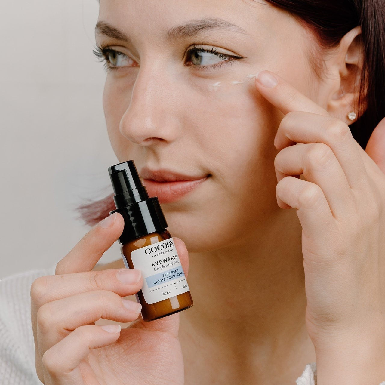 Oh Canada Gifts model applying Eyewaken eye cream from a small brown glass pump bottle to her under-eye area.