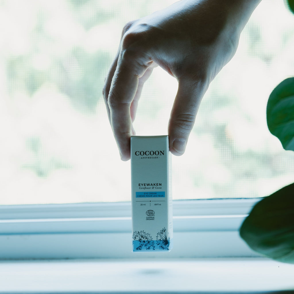 Oh Canada Gifts Eyewaken eye cream box held by a hand against a bright window, showcasing organic skincare packaging.
