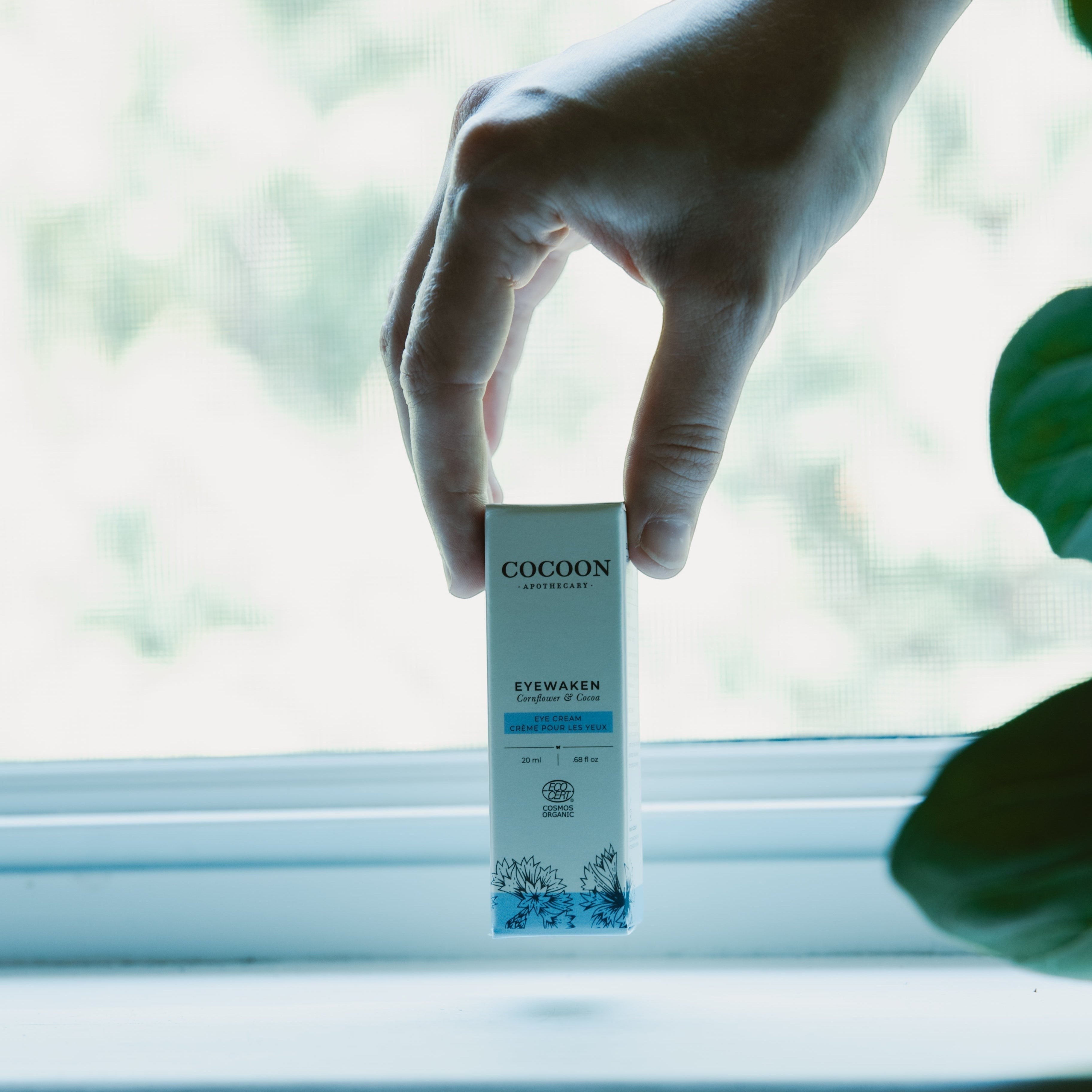 Oh Canada Gifts Eyewaken eye cream box held by a hand against a bright window, showcasing organic skincare packaging.