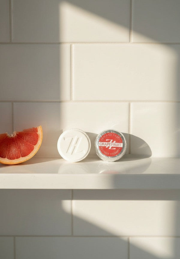 Oh Canada Gifts Zen & Hearth grapefruit shower steamers with a fresh grapefruit slice on a white tiled shower shelf.