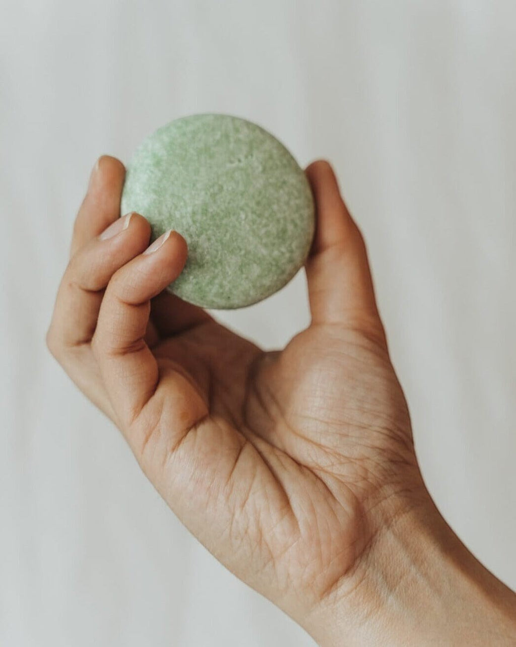 Oh Canada Gifts round green peppermint and eucalyptus shampoo bar held in a hand