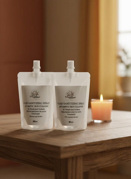 Oh Canada Gifts 200ml unscented hand sanitizing spray refill pouches on a wooden table with a lit candle.