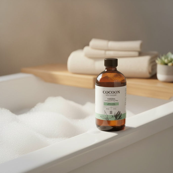 Oh Canada Gifts Kahuna bubble bath in a glass bottle next to a foamy bathtub with towels in the background.