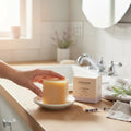 Oh Canada Gifts Lavandin Bar Soap on a white dish next to its beige packaging on a wooden bathroom counter.