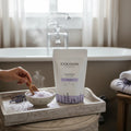 Oh Canada Gifts lavender bath salts in a pouch and bowl with a wooden scoop, set in a relaxing bathroom scene.