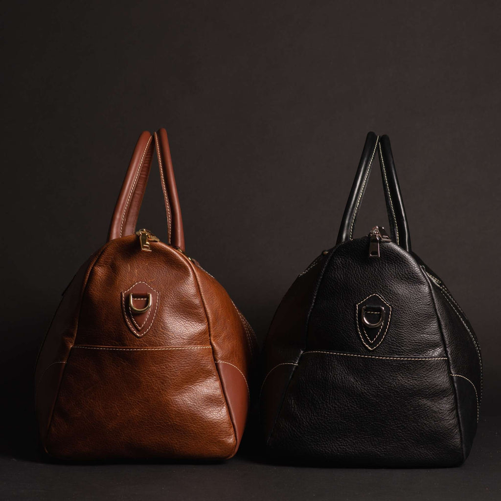 Oh Canada Gifts handcrafted full-grain leather duffle bags in brown and black side by side on a dark background.