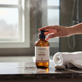 Oh Canada Gifts Malechemy facial cleanser in an amber glass bottle with a pump, set in a steamy bathroom.