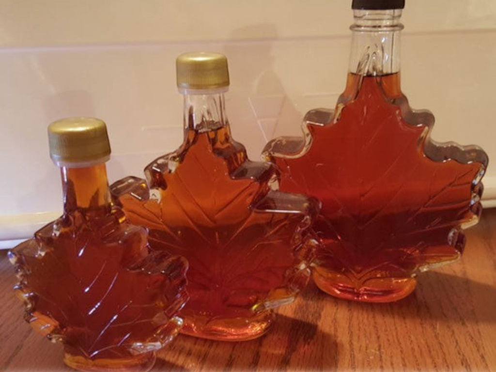 Oh Canada Gifts organic maple syrup in three iconic maple leaf-shaped glass bottles of varying sizes.