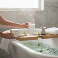 Oh Canada Gifts Mint Eucalyptus bath cube held over a steaming bathtub with botanical accents on a wooden tray.