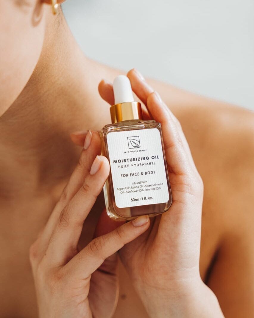 Oh Canada Gifts Zero Waste MVMT moisturizing oil in a glass dropper bottle held by a woman for face and body care.