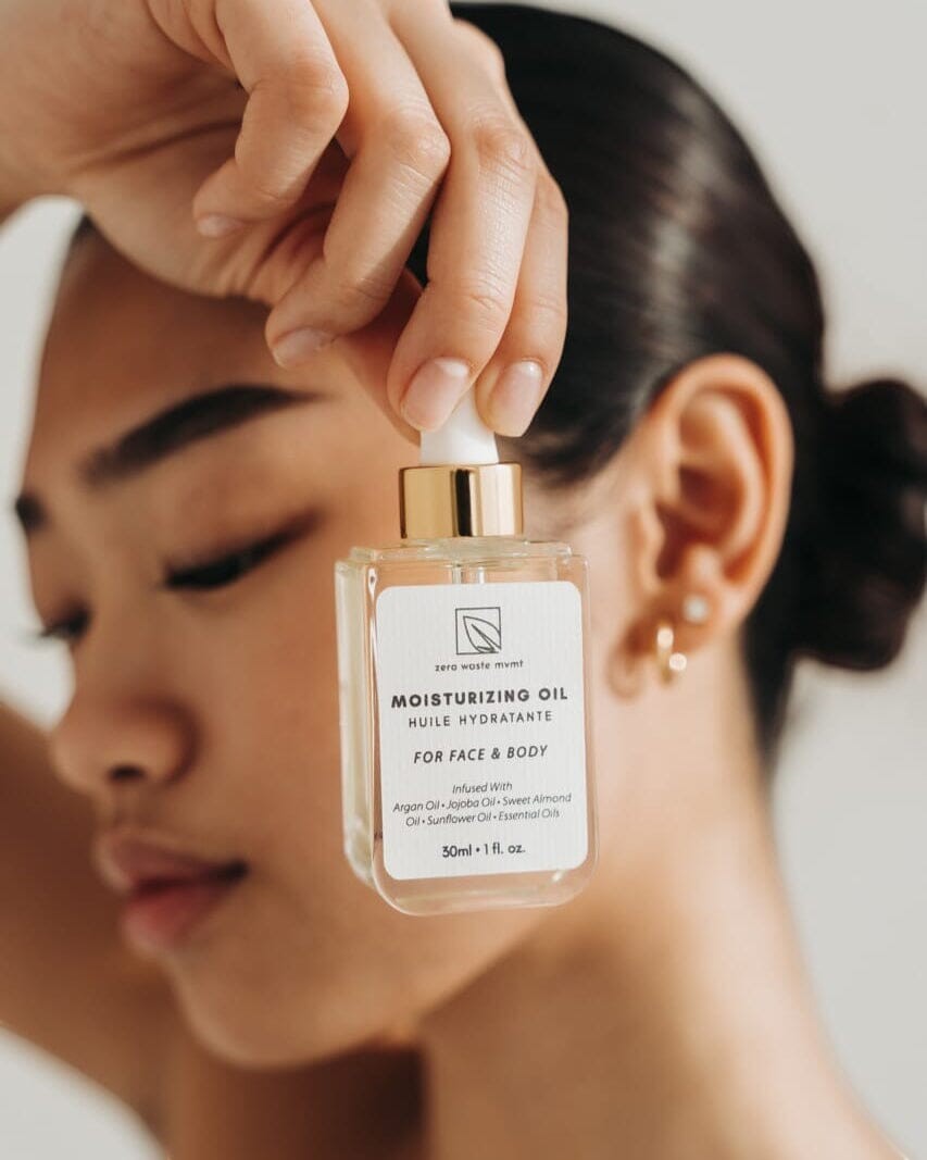Oh Canada Gifts Zero Waste MVMT moisturizing oil in a glass dropper bottle held by a woman for face and body care.