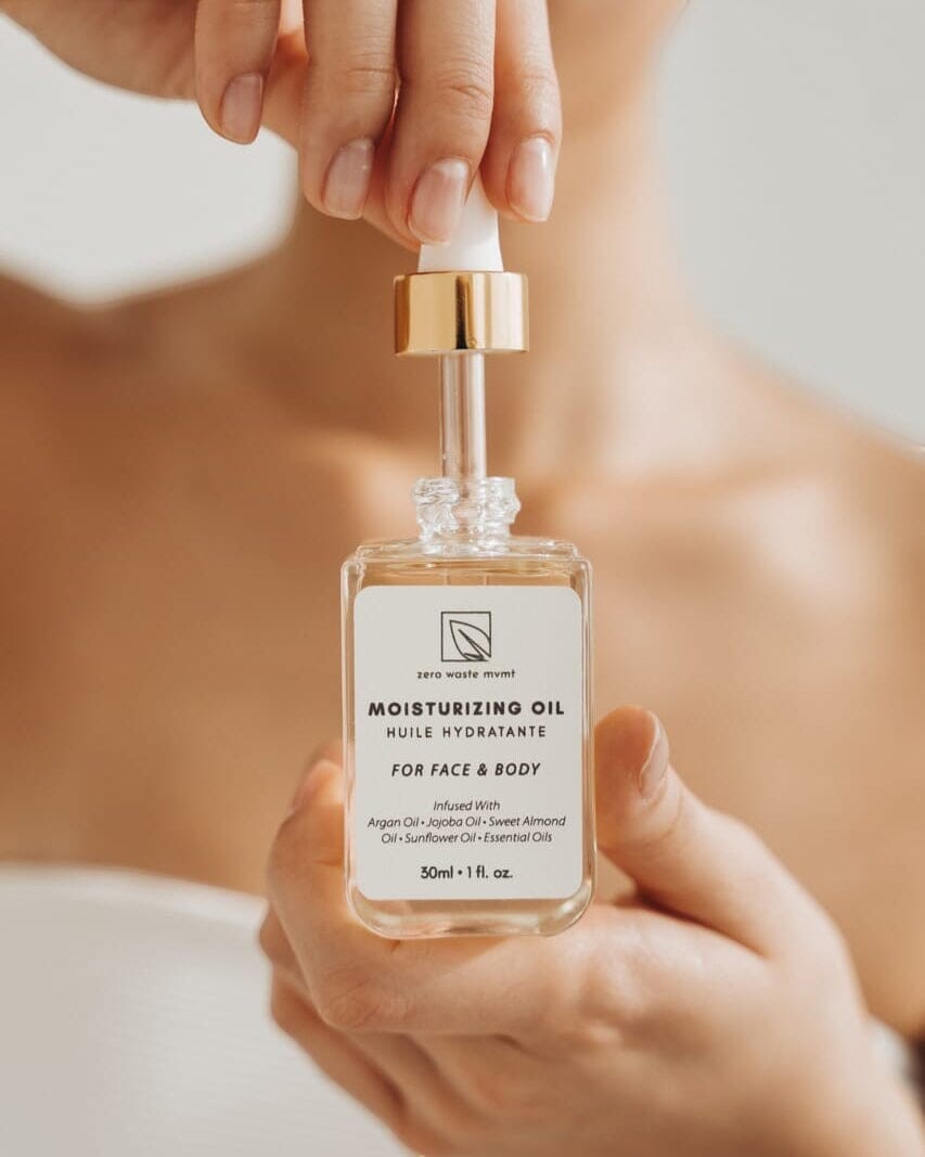 Oh Canada Gifts Zero Waste MVMT moisturizing oil in a glass dropper bottle held by a person for face and body care.