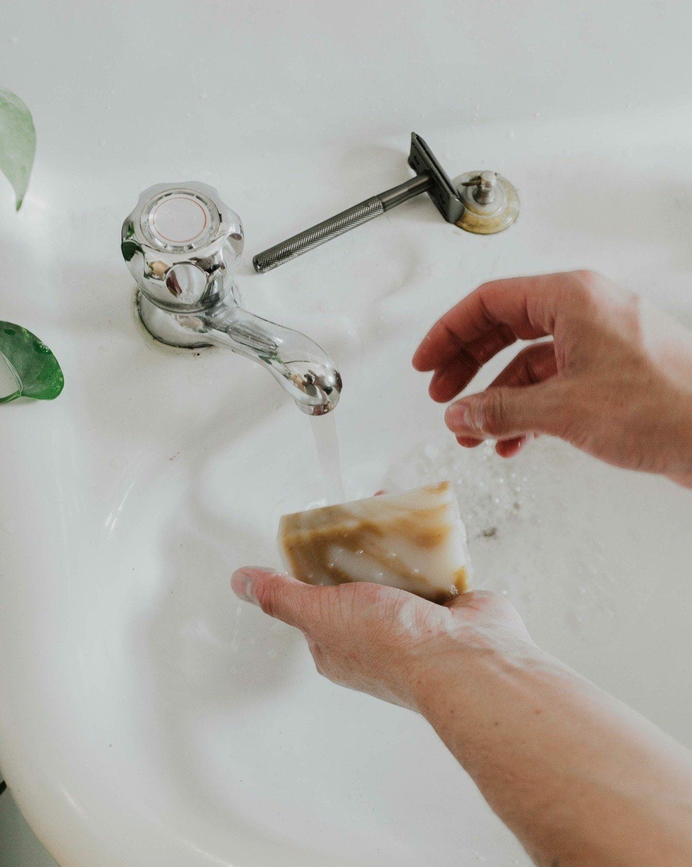 Oh Canada Gifts natural shave bar being held under running water in a bathroom sink with a safety razor nearby