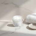 Oh Canada Gifts Cream It nourishing whipped facial moisturizer in a glass jar on a marble surface with a white towel.