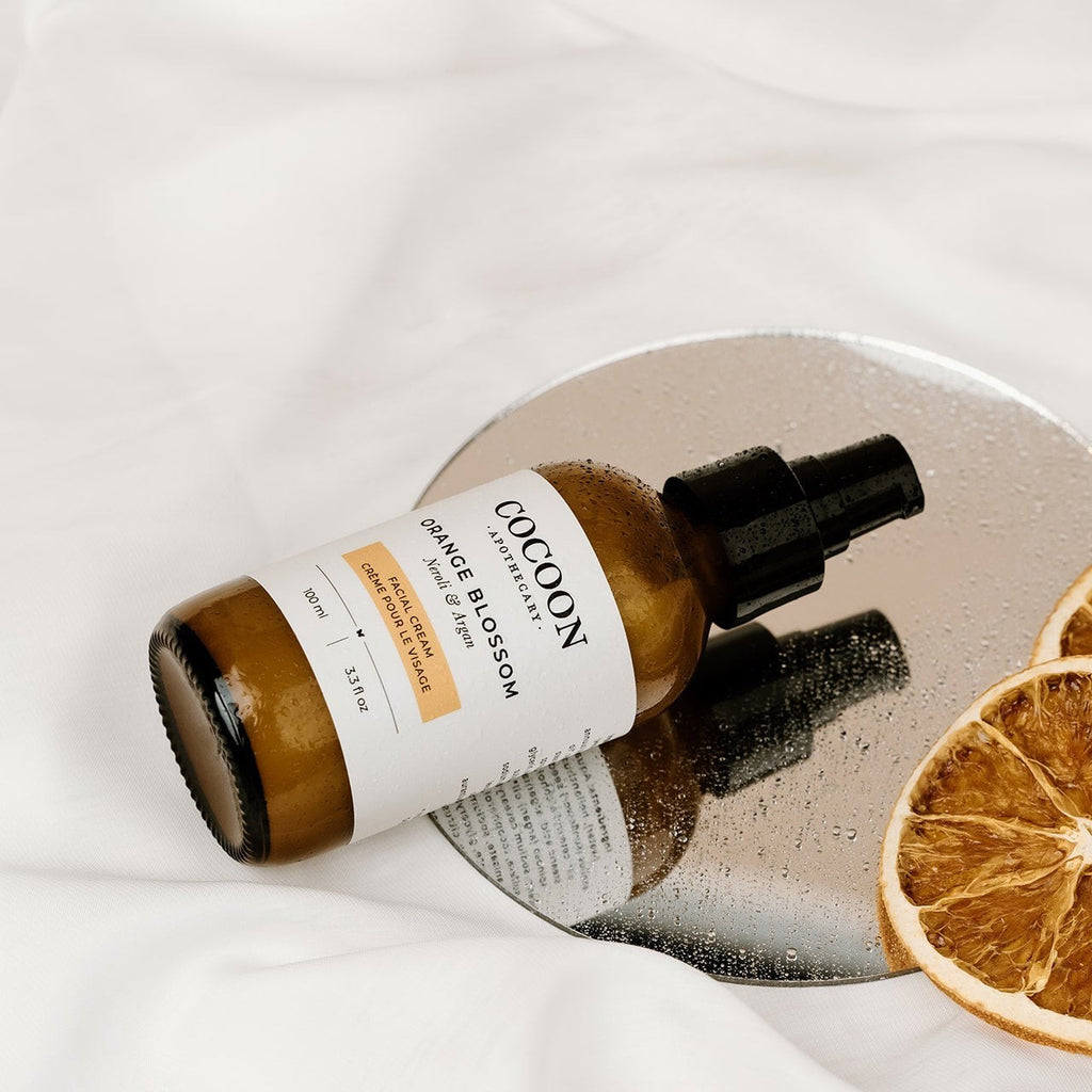 Oh Canada Gifts Cocoon Apothecary Orange Blossom facial cream in a glass bottle on a mirror with dried orange slices.