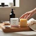 Oh Canada Gifts Cocoon Apothecary patchouli bar soap with its white and pink box on a wooden tray with a hand.