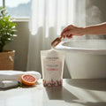 Oh Canada Gifts Patchouli Vibes bath salts in a pouch with a wooden scoop, fresh grapefruit, and a steaming bathtub.