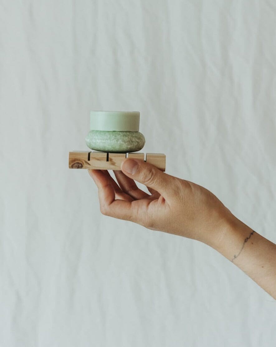Oh Canada Gifts peppermint and eucalyptus shampoo bar resting on a small wooden soap dish held in a hand.