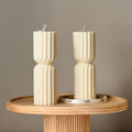 Two Oh Canada Gifts small ribbed hourglass soy wax pillar candles standing on a round wooden pedestal.