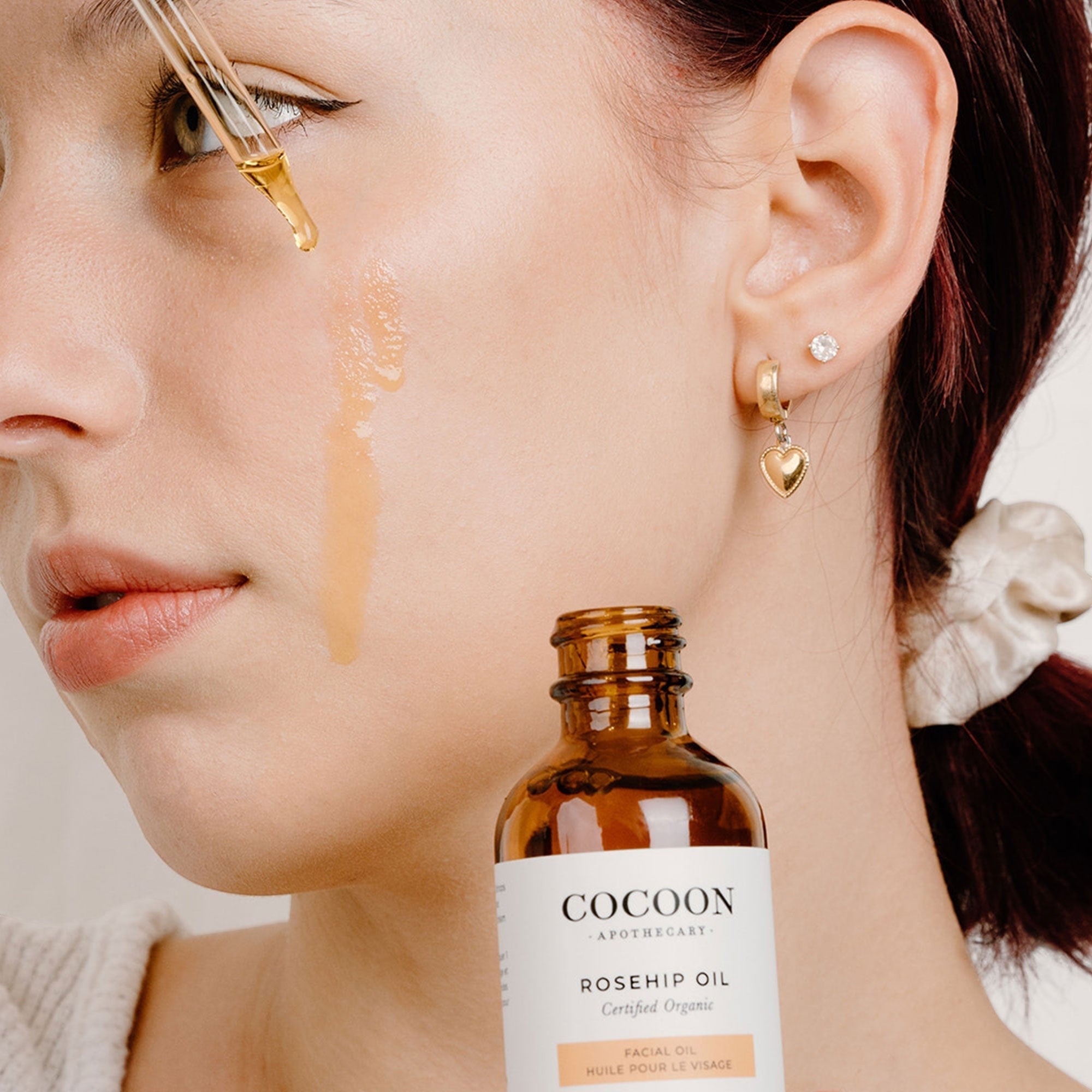Oh Canada Gifts Cocoon Apothecary rosehip facial oil being applied with a glass dropper to a woman's cheek