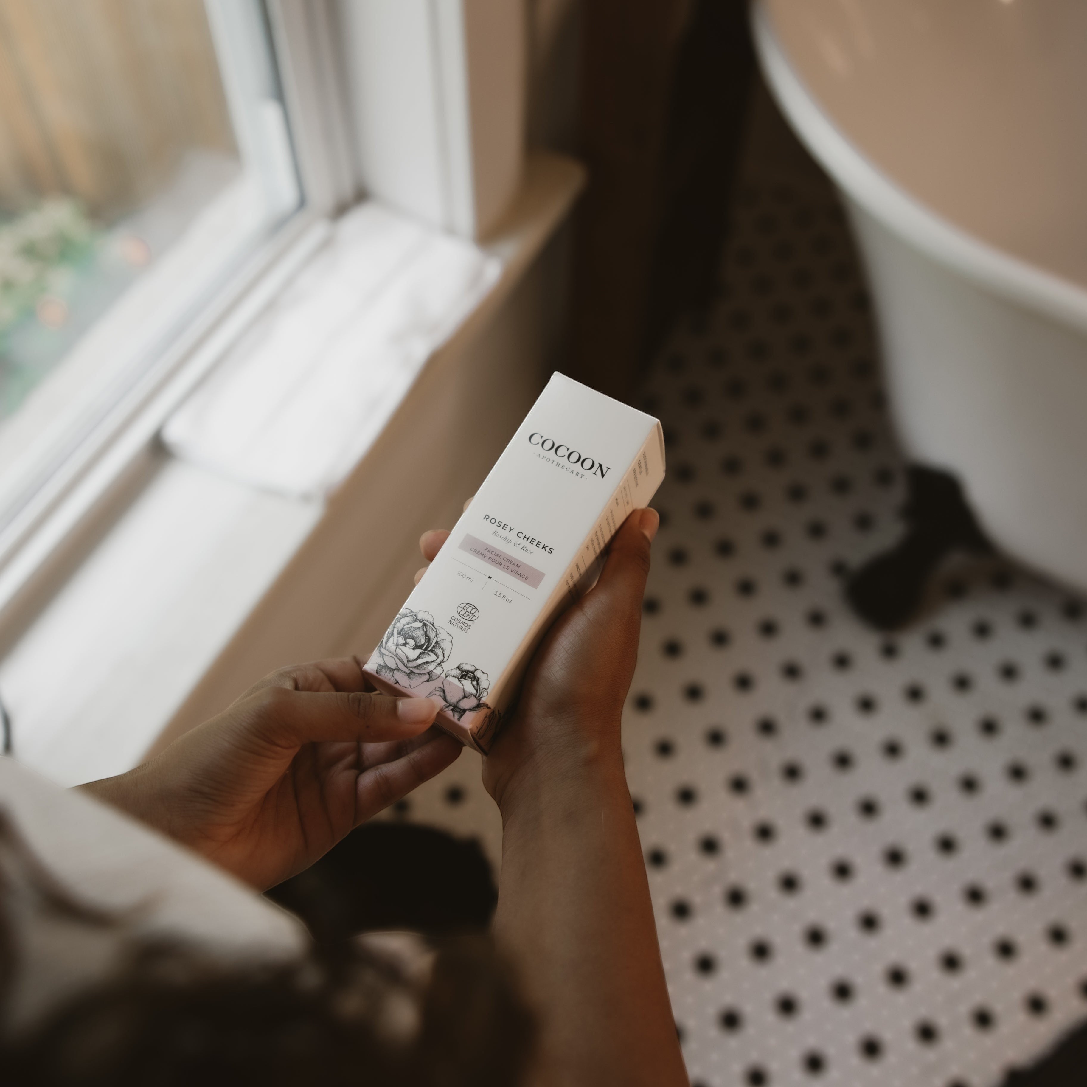 Oh Canada Gifts Rosey Cheeks facial cream box held in hands in a bright bathroom setting