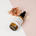 Oh Canada Gifts Rosey Cheeks facial cream in an amber glass pump bottle with a floral accent on a two-tone background.