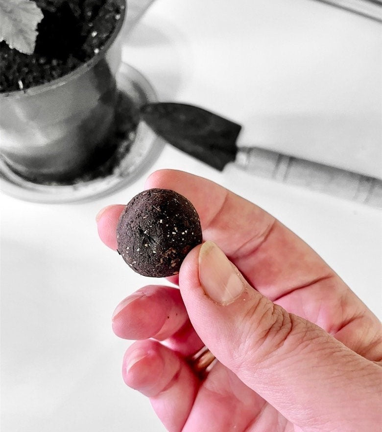 Oh Canada Gifts DIY seed bomb made of dark soil and recycled paper held in a hand with a small trowel in the background