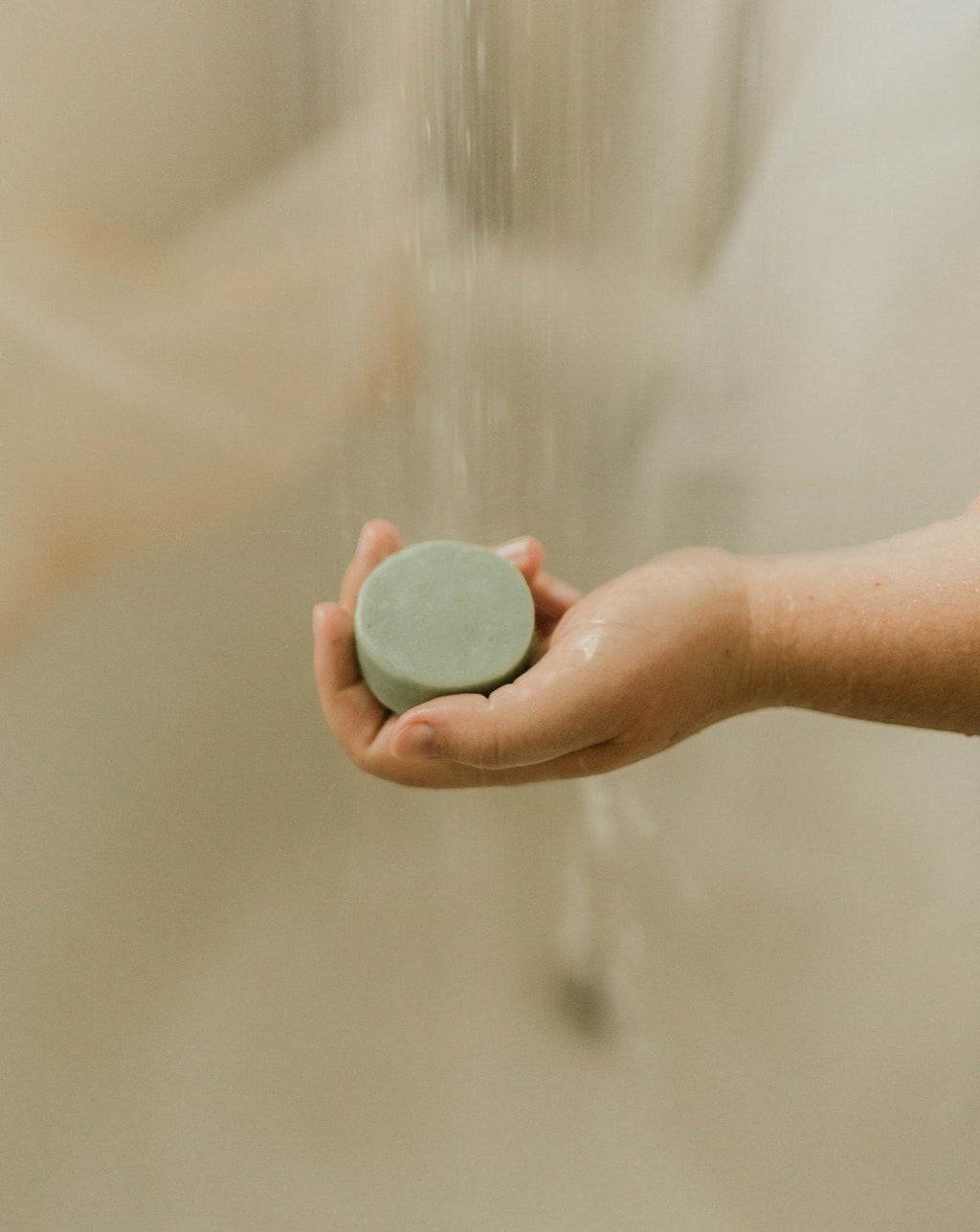 Oh Canada Gifts peppermint and eucalyptus solid conditioner bar held under a shower stream