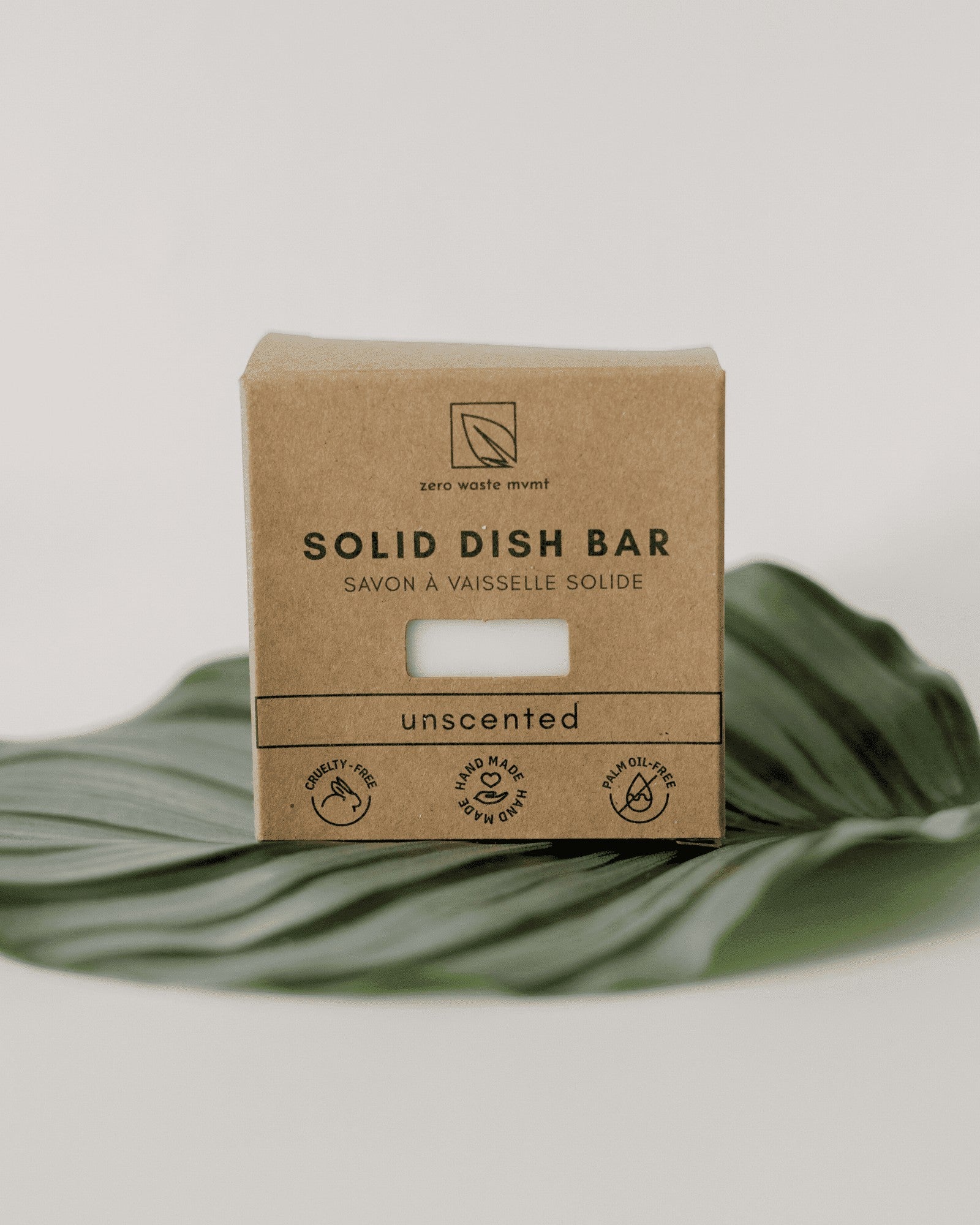 Oh Canada Gifts zero-waste solid dish soap bar in eco-friendly brown paper packaging resting on a large green leaf.