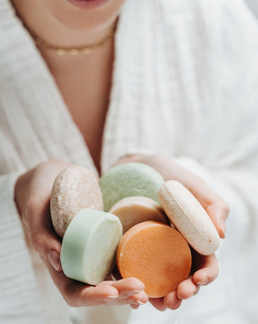 Oh Canada Gifts collection of round solid conditioner and shampoo bars held in hands, featuring various pastel colors.