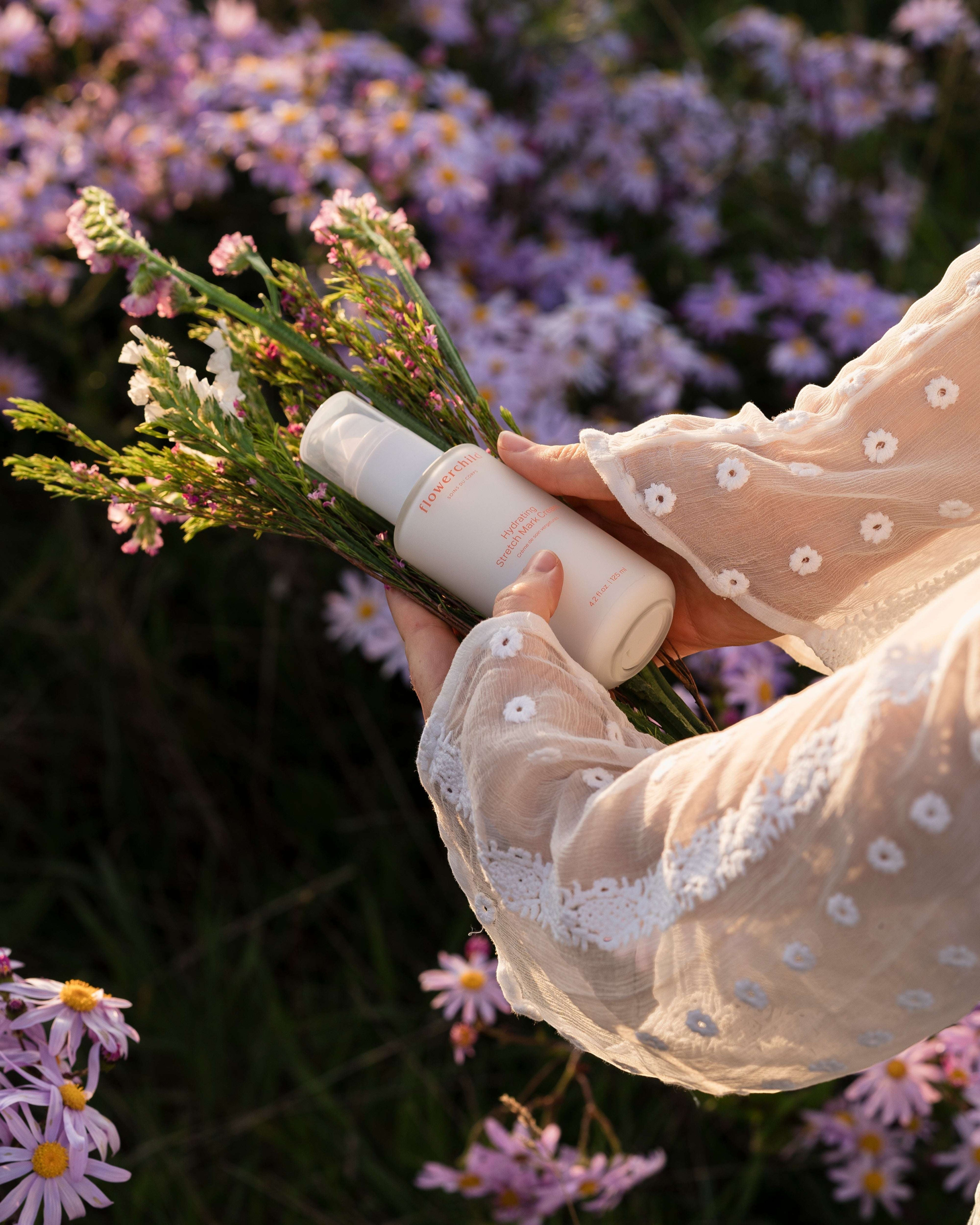 Oh Canada Gifts Flowerchild stretch mark cream held by hands in a floral field, promoting pregnancy skin care.